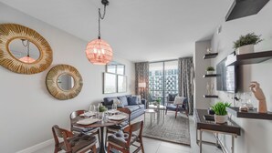 A modern living room with a dining area, large windows, and a TV on the wall. - 5350 Nw Downtown - Doral Building - We Host (Miami)