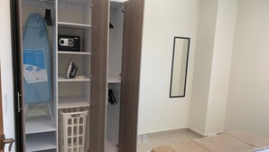 A bedroom with a bed, a wardrobe with open doors revealing shelves and a laundry basket, and a mirror on the wall.