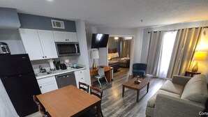 Kompakti hotellihuone, jossa on pieni keittiö, ruokailutila, oleskelutila sohvalla, televisio ja sänky.