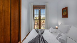 Une chambre d’hôtel avec un lit, une fenêtre avec des rideaux, une lampe fixée au mur et une affiche.