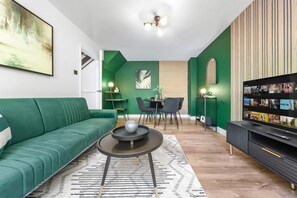 Un salon moderne avec un canapé vert, une table basse ronde, un téléviseur et un coin repas comprenant des chaises et une table.