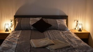 Un letto rifatto con biancheria a fantasia, due abat-jour e un cuscino decorativo scuro.