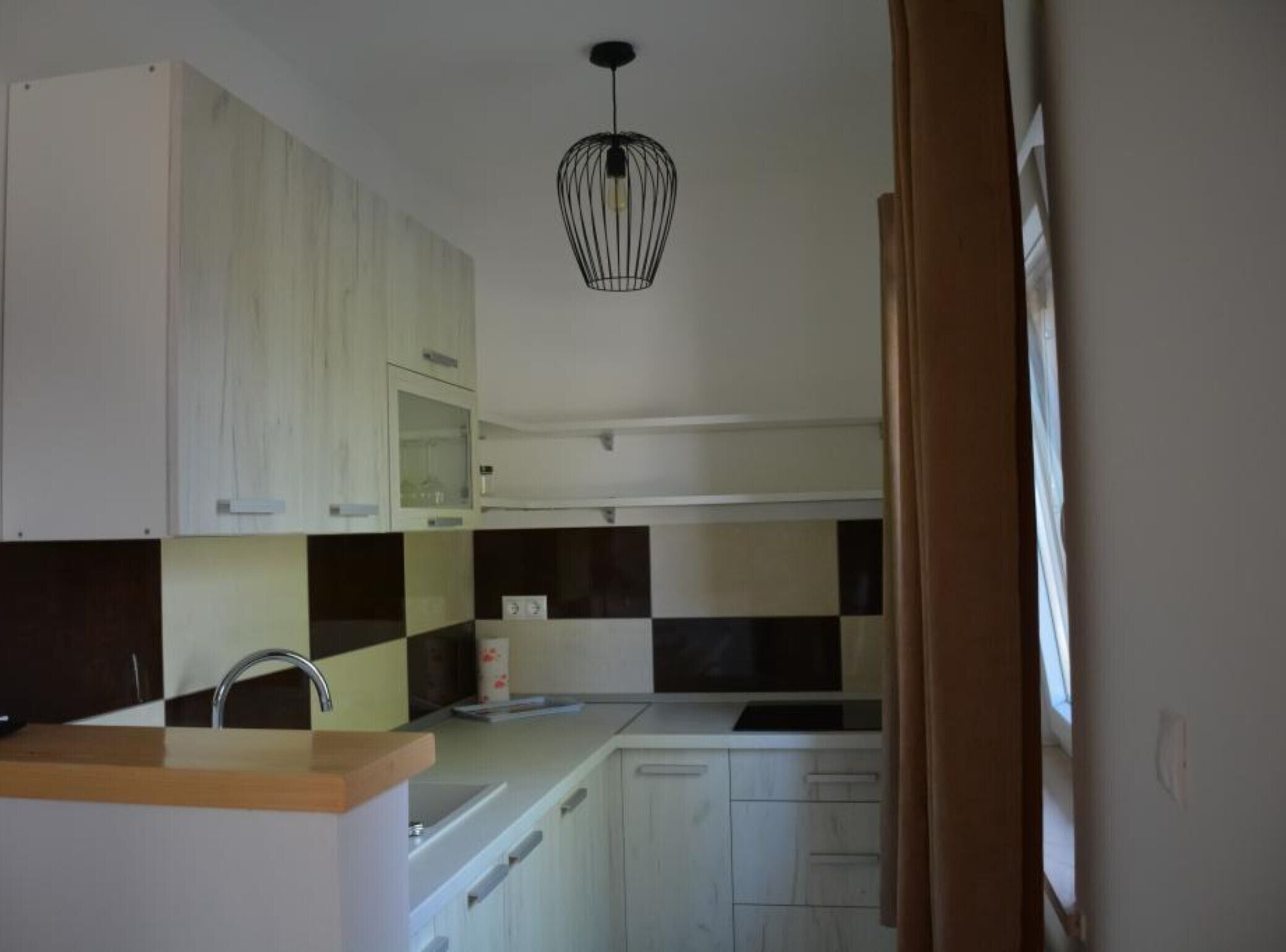 Een keuken met witte kasten, een zwart-wit geruit spatwand, een houten aanrecht en een hangende lamp.