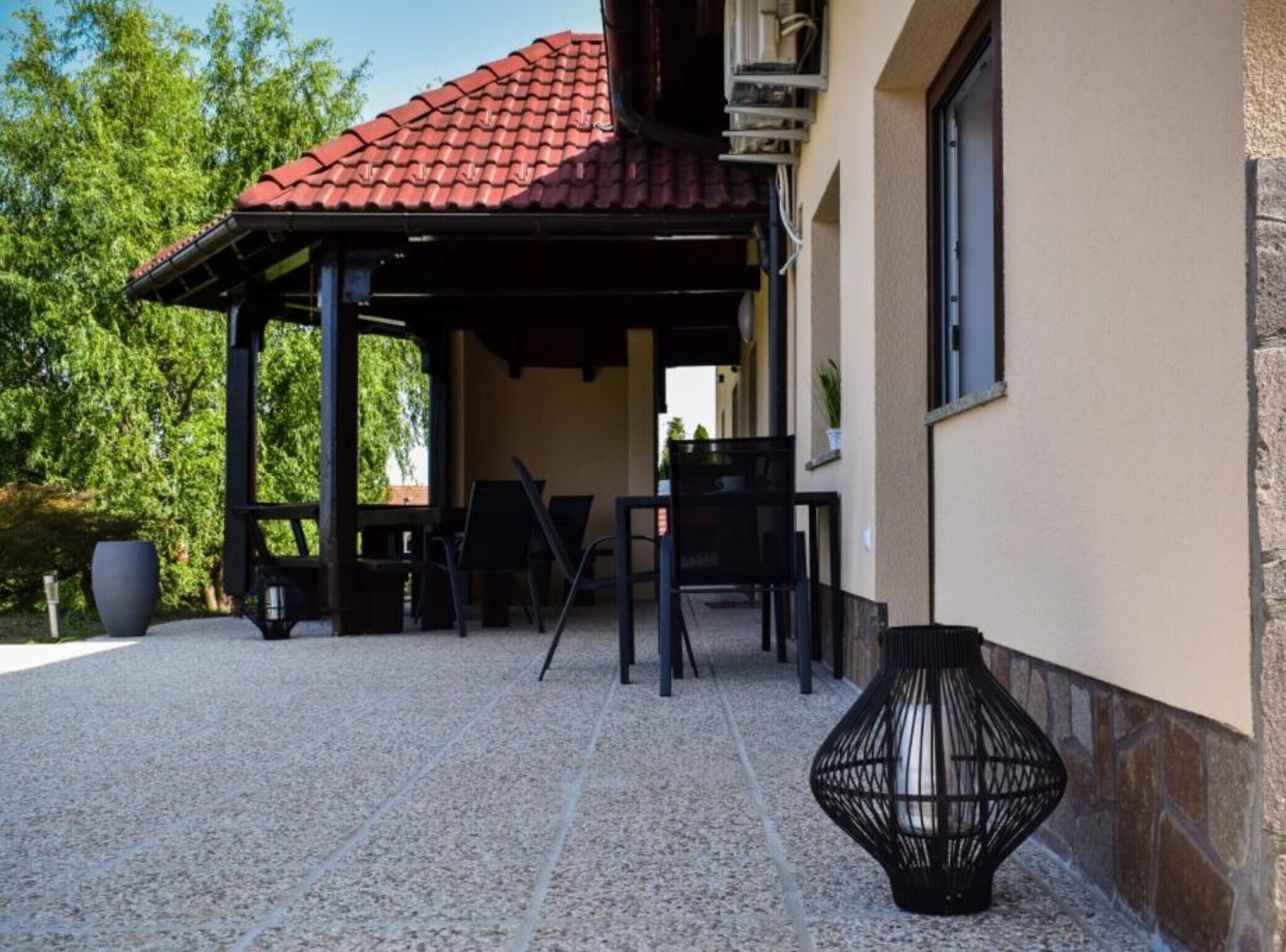 An outdoor patio with a red-tiled roof, a pergola, and a seating area with chairs and a table.