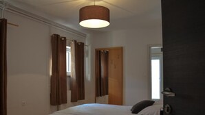 A bedroom with a bed, a hanging light fixture, and a door with a coat rack.