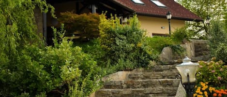 A house with a sloped roof, stone steps, and a garden with various plants and flowers.