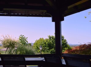 A covered outdoor seating area with benches and a lamp post, overlooking a park with trees and distant mountains. - Zevnik Quiet Retreat with Stunning Views and Equestrian Activities - Triple Room with Private Bathroom (Brežice)