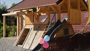 Eine Holzhütte mit rotem Ziegeldach, einer Holzterrasse und einer Rutsche.