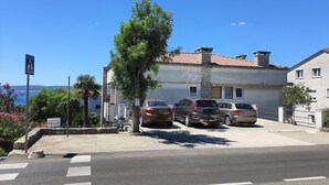 A residential building with a stone facade, parked cars, and a clear view of the sea. - Fashonable and Trendy Apartments Crikvenica - Studio Apartment with Balcony (Crikvenica)