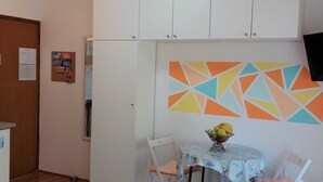 A compact room with a kitchenette, a dining area with a table and chairs, and a colorful geometric wall decoration. - Fashonable and Trendy Apartments Crikvenica - Studio Apartment with Balcony (Crikvenica)