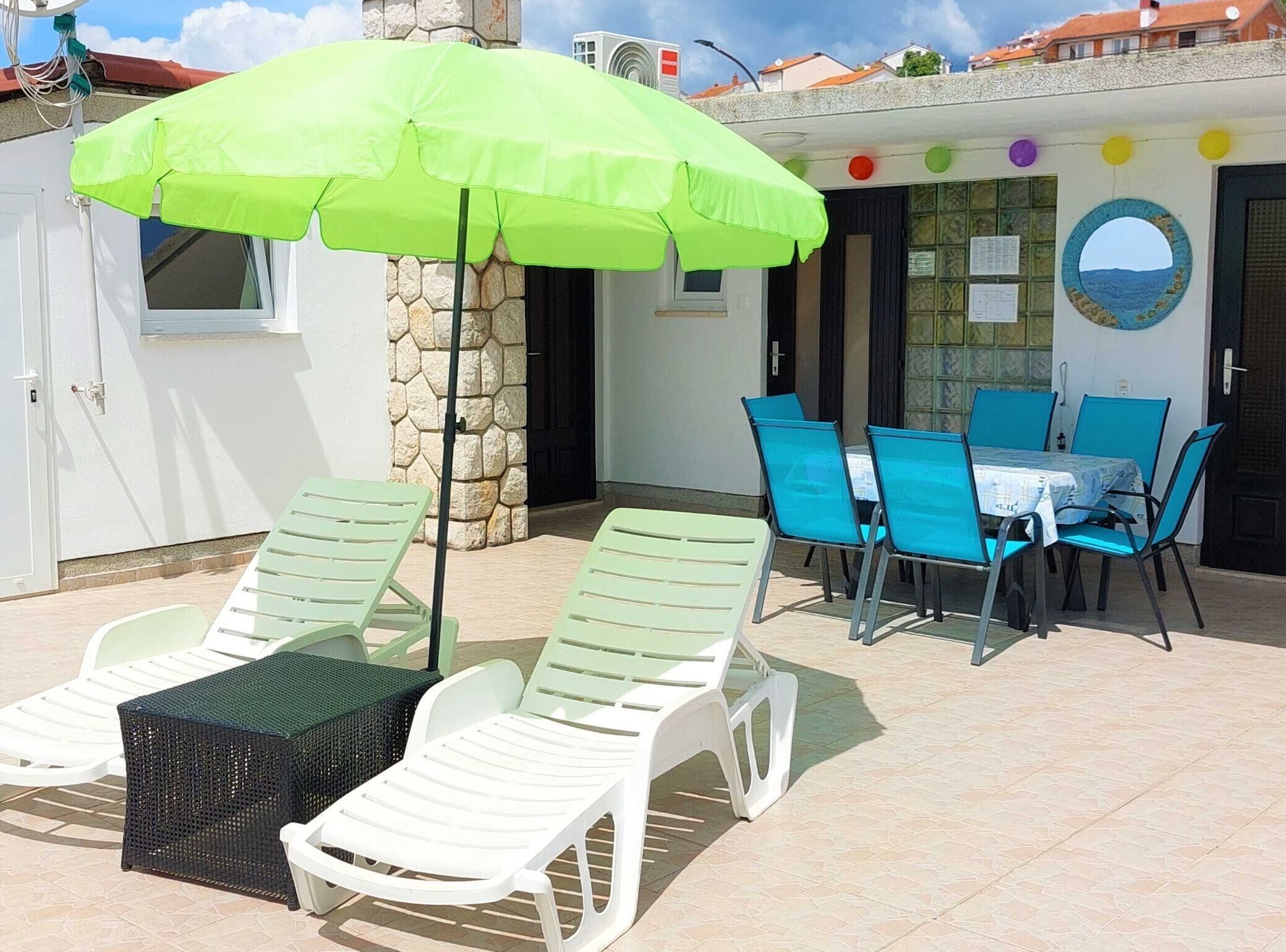 A patio with sun loungers, a table with chairs, and a green umbrella.