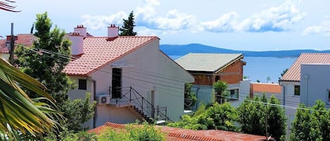 A coastal residential area with houses featuring red-tiled roofs and white walls, surrounded by greenery and overlooking a body of water.