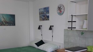 Ein Schlafzimmer mit einem Bett, einem Schreibtisch mit Laptop, einer Wanduhr und einem Gemälde.