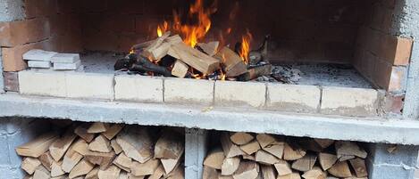 A brick fireplace with a fire burning inside, surrounded by stacked firewood.
