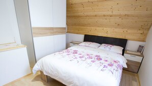 Un dormitorio con cabecera de madera, cama con ropa de cama floral, mesita de noche y una mesita con un cuadro enmarcado.