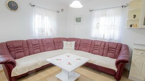 Una sala de estar con un amplio sofá rojo en forma de L, una mesa de centro blanca con diseños florales y un mueble blanco con espejo.