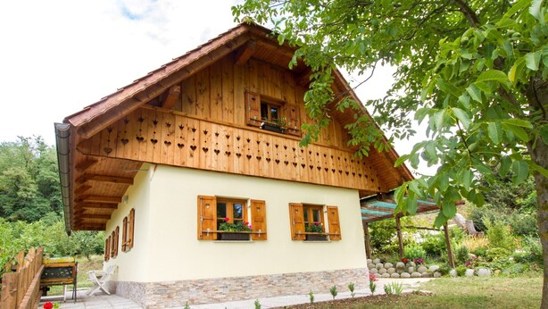 Una cabaña de madera con techo inclinado, varias ventanas con contraventanas y base de piedra.