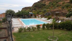 Une piscine dotée de chaises longues et d’une pergola, entourée d’une pelouse et avec des collines en arrière-plan.