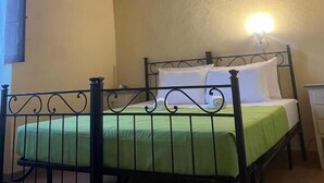 Un lit simple avec une couvre-lit verte, un plafond en bois et un luminaire fixé au mur.
