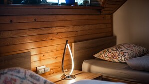 Um quarto de cabana de madeira aconchegante, com uma cama, uma mesinha e uma luminária, e uma janela.