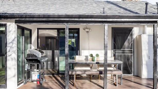 Een modern terras buiten, met een barbecue, een zithoek en een glazen deur naar binnen.