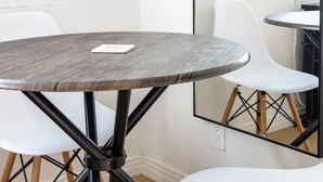 Een ronde tafel met een houten blad en zwarte metalen poten, vergezeld van twee witte stoelen met houten poten.
