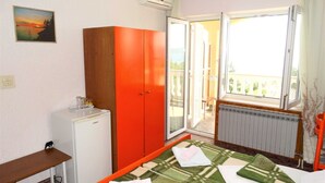 Ein Zimmer mit einem Bett, einem Schrank, einem kleinen Kühlschrank, einem Fenster und einer Heizung.