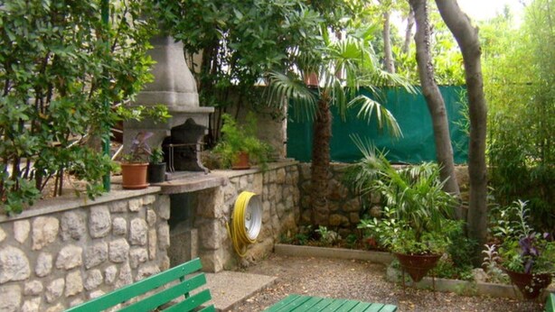 A stone wall with a green bench and a small table in a garden area with potted plants and a hose reel. - Crikvenica Apartments and Rooms with Sea View - One Bedroom Apartment with Sea View (Crikvenica)