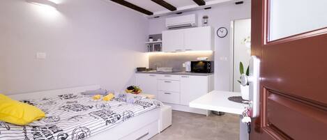 A compact bedroom with a bed, bedside table, and a small kitchenette.