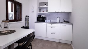 Une cuisine compacte avec des meubles blancs, un four à micro-ondes, une bouilloire et un petit plan de travail.