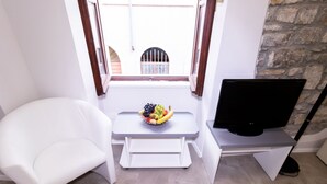 Une petite pièce moderne, avec une chaise blanche, une petite table sur laquelle se trouve un panier de fruits et un téléviseur à écran plat posé sur un meuble.