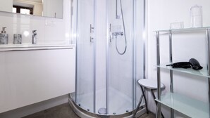 Une salle de bain moderne dotée d’une douche à parois de verre, d’un meuble-lavabo blanc avec un miroir et d’une étagère en verre où sont rangés les articles de toilette.