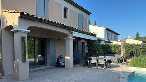 Un patio con piscina, mobiliario exterior y una zona de estar cubierta.