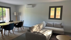 Una sala de estar moderna con un sofá, una mesa de centro, una mesa de comedor con sillas y un ventanal con vistas a zonas verdes.