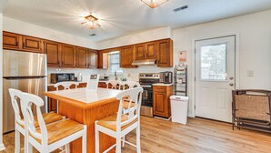 A modern kitchen with wooden cabinets, stainless steel appliances, a central island with chairs, and pendant lighting. - Deck & Fenced Yard: Family Home in Winterville (Winterville)