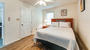 A bedroom with a bed, a ceiling fan, a window with blinds, a nightstand, and a door. - Deck & Fenced Yard: Family Home in Winterville (Winterville)