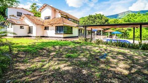 Una casa de dos pisos con techo de tejas, piscina y un patio cubierto.