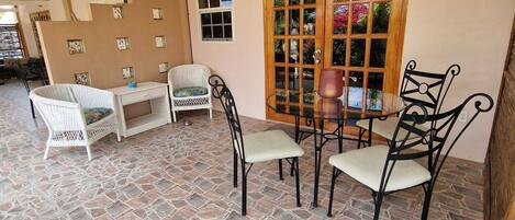 A covered patio area with stone flooring, white wicker furniture, and a wooden door with glass panels.