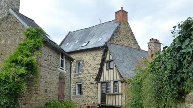 A narrow cobblestone street with traditional stone buildings, one with a visible window and a red door. - Le Manoir de la Magdeleine (Lanvallay)