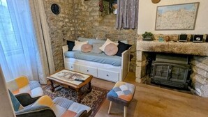 A cozy living room with a stone wall, a fireplace, a sofa with cushions, a coffee table, and a small ottoman. - Le Manoir de la Magdeleine (Lanvallay)