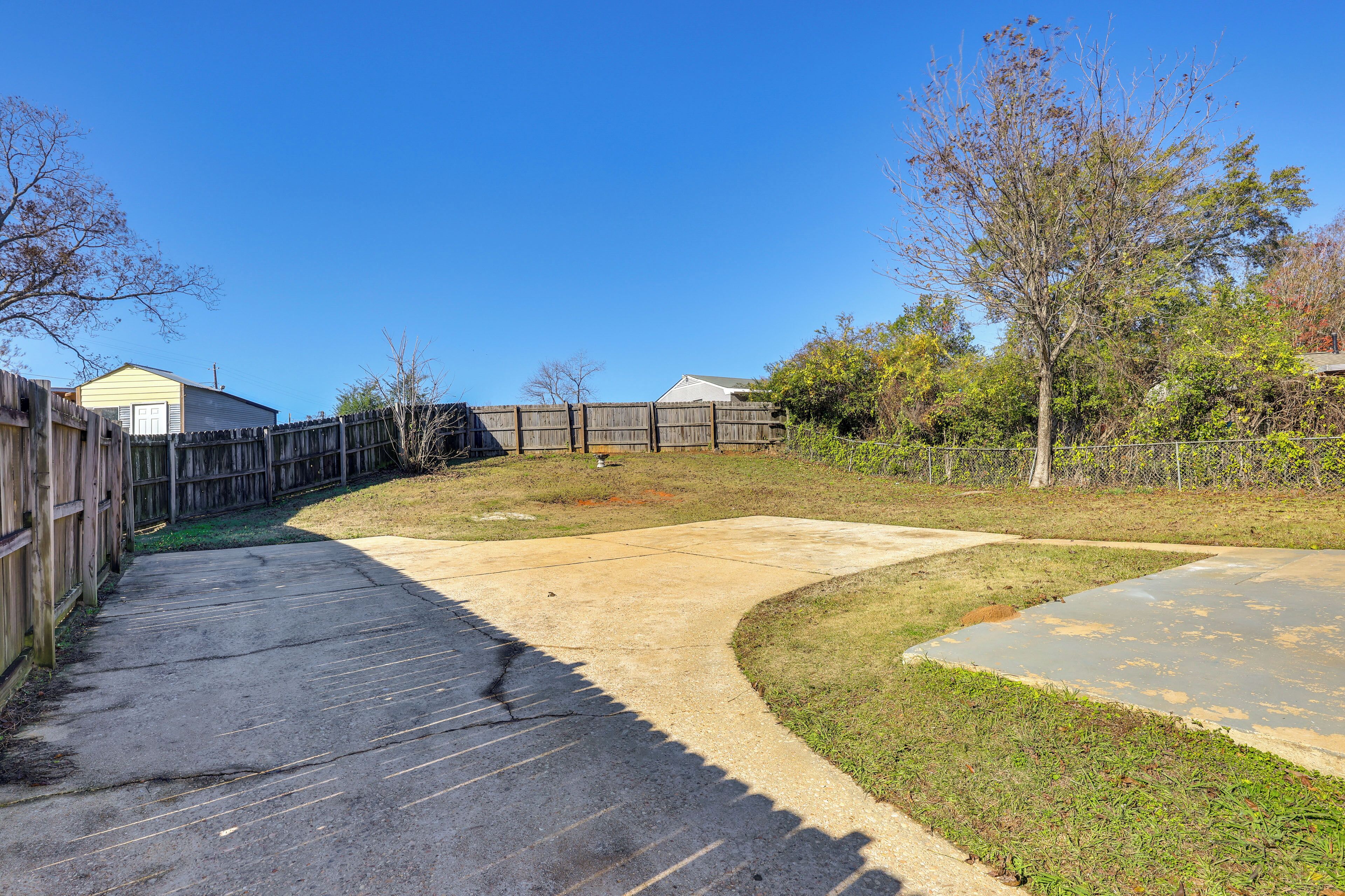 Un jardin avec un chemin en béton, une clôture en bois et une pelouse.