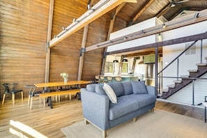 Una habitación amplia con techo alto, vigas de madera, un sofá, una mesa de comedor y una escalera.