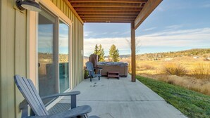 Un porche cubierto con un jacuzzi, dos sillas Adirondack y vistas a un paisaje rural.