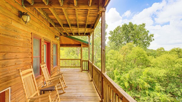A wooden cabin with a porch, rocking chairs, and a view of a forest. - Spacious Cabin w/ Views, Near Lake Lawtonka! (Medicine Park)