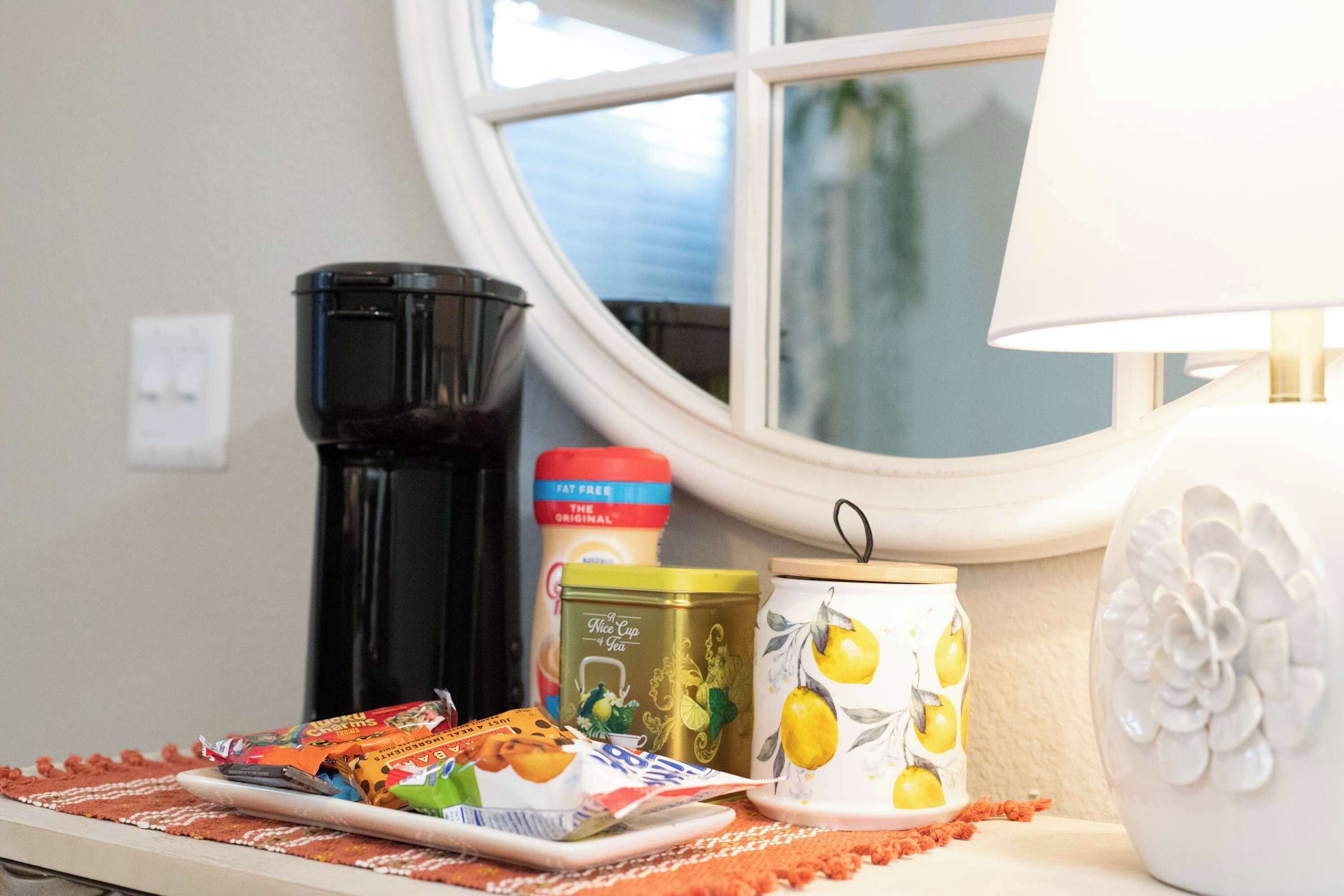 A kitchen counter with a coffee maker, a can of tea, a mug with lemon prints, and a decorative plate.