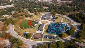 Vista aérea de un complejo deportivo con un campo de béisbol, varios edificios y zonas de estacionamiento.