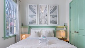 Una cama bien hecha con sábanas blancas, un cabecero con diseño geométrico y una puerta color turquesa.