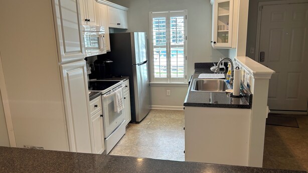 A kitchen with white cabinets, a black refrigerator, a stainless steel sink, and a window with blinds. - Charming 2-bedroom building in fabulous Augusta with AC, WiFi (Augusta)