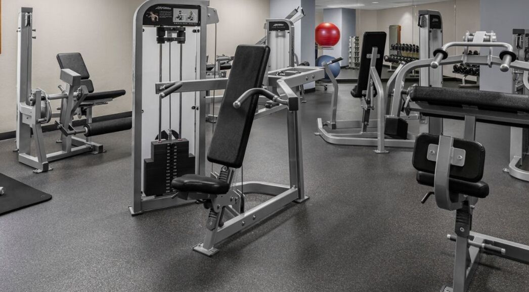 Un gimnasio con diferentes máquinas de ejercicio, incluyendo una prensa de banca, una prensa de piernas y máquinas de poleas.