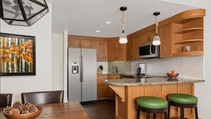 Una cocina moderna con armarios de madera, encimera de granito, microondas integrado y una zona de bar con taburetes.
